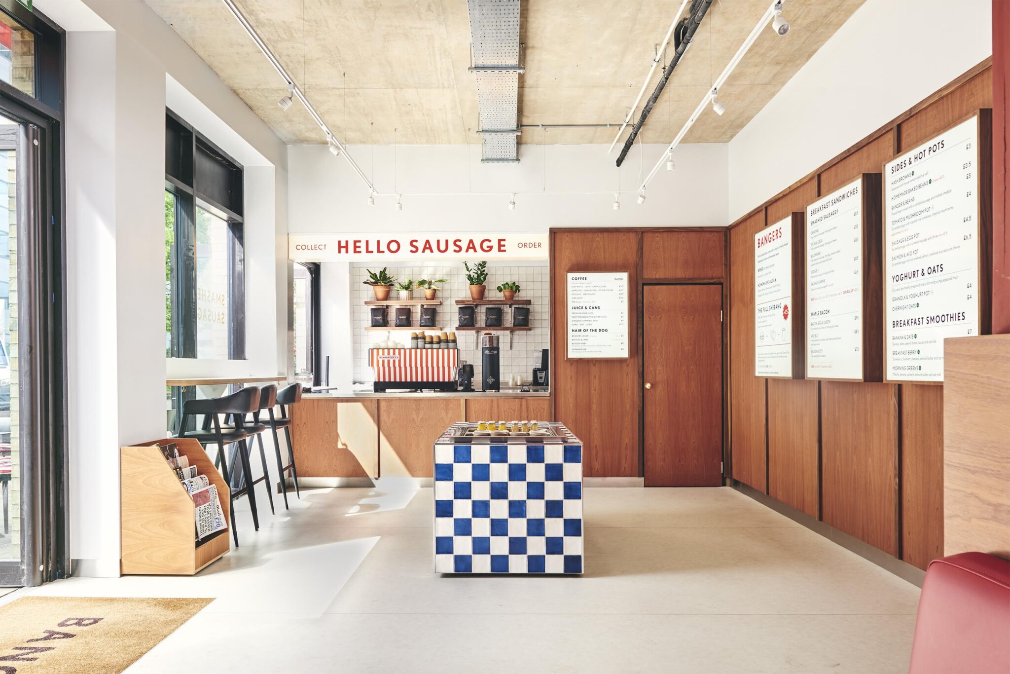 Modern breakfast bar interior with wood paneling, blue checkered counter, and "HELLO SAUSAGE" signage on white tiled wall.