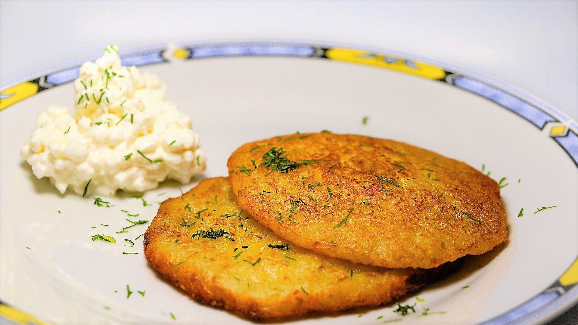 Golden potato latkes garnished with fresh herbs served alongside a dollop of sour cream on a decorative plate.