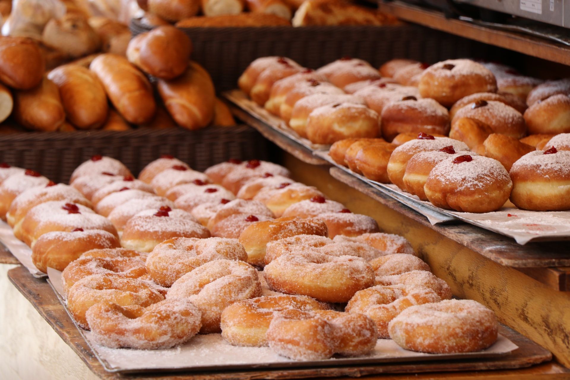 Fresh sufganiyot donuts dusted with powdered sugar displayed on bakery trays, some filled with jam.