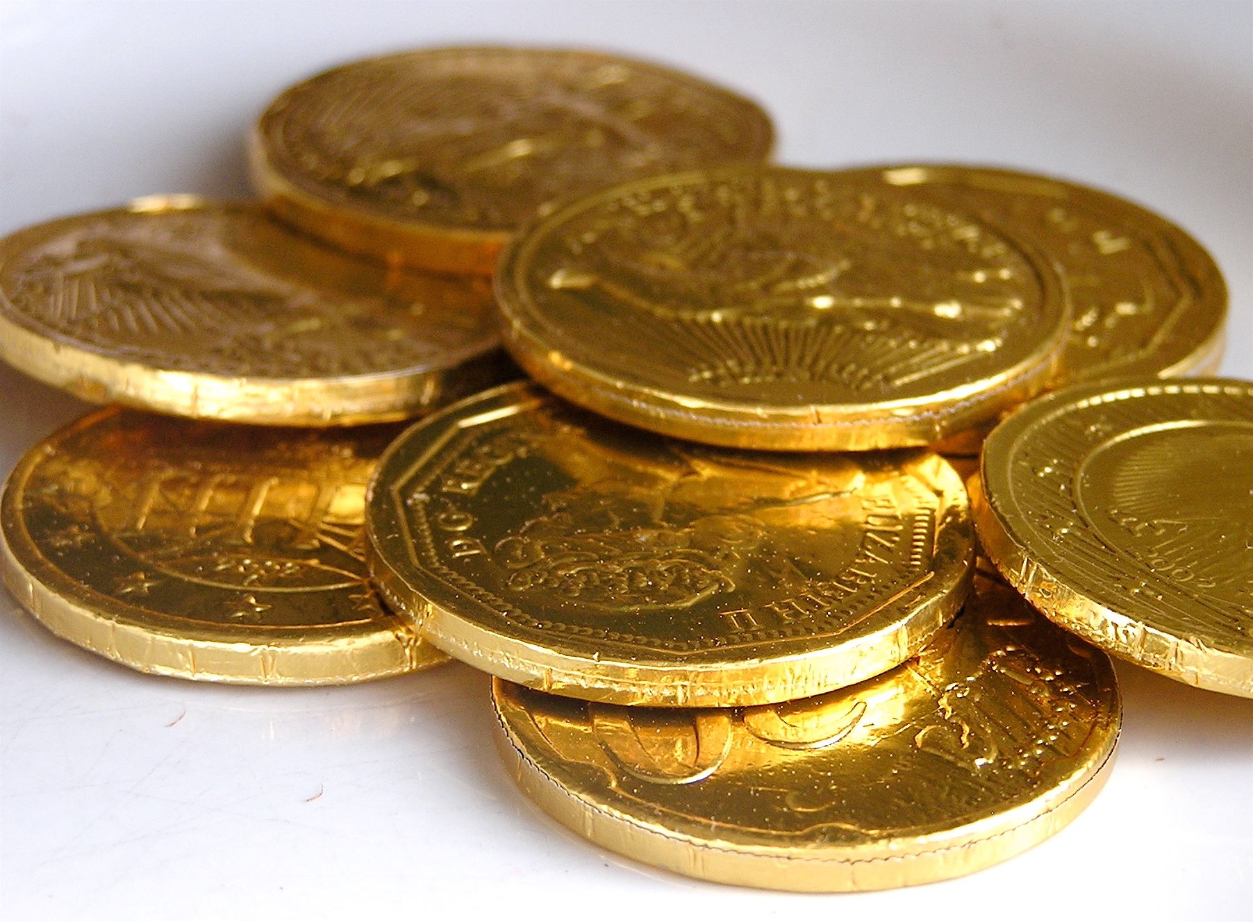 Golden foil-wrapped chocolate coins scattered on a white surface, traditional Hanukkah gelt with embossed designs.
