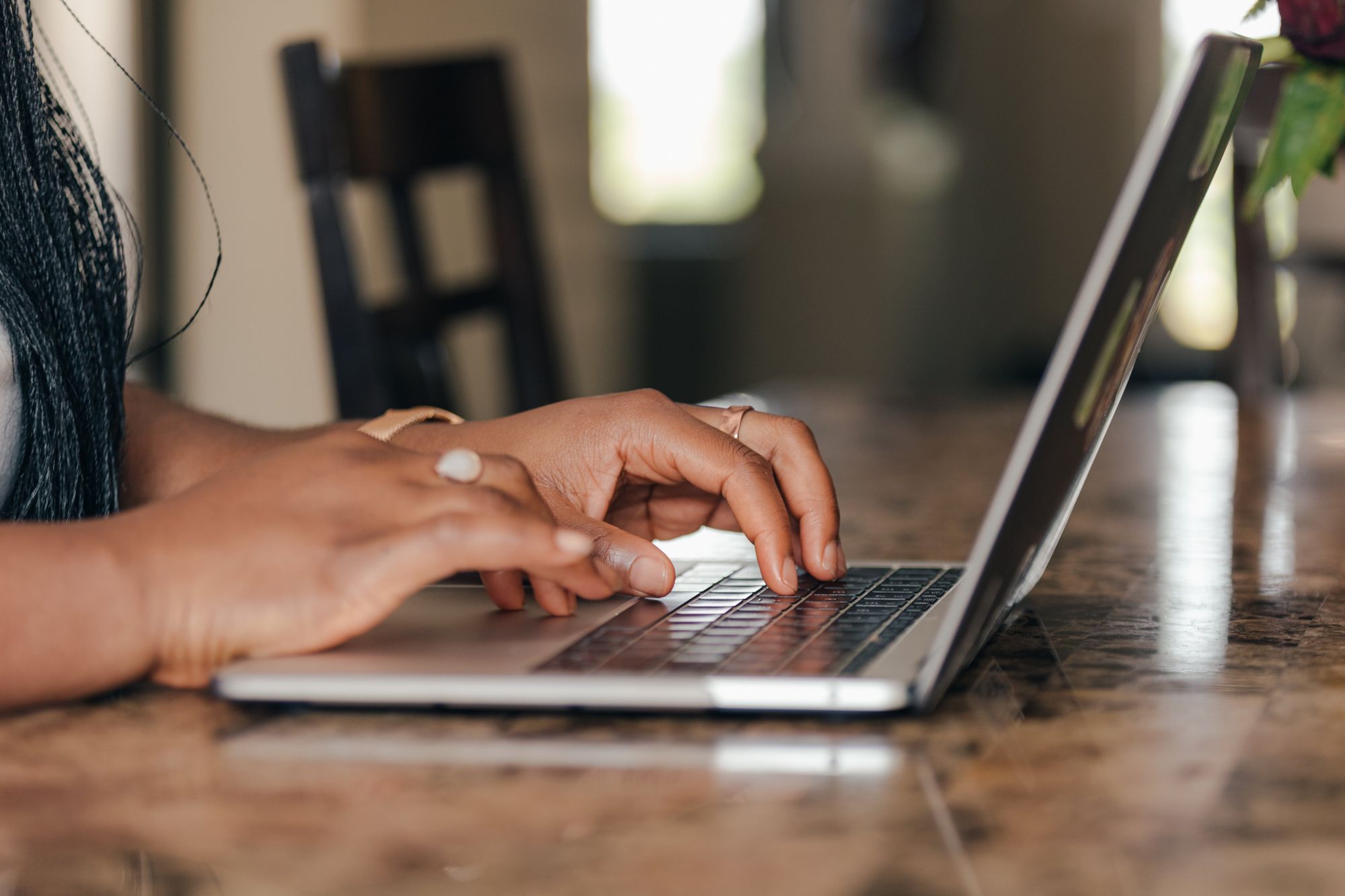 Person typing on laptop at wooden table, working on creating an online business presence from home.