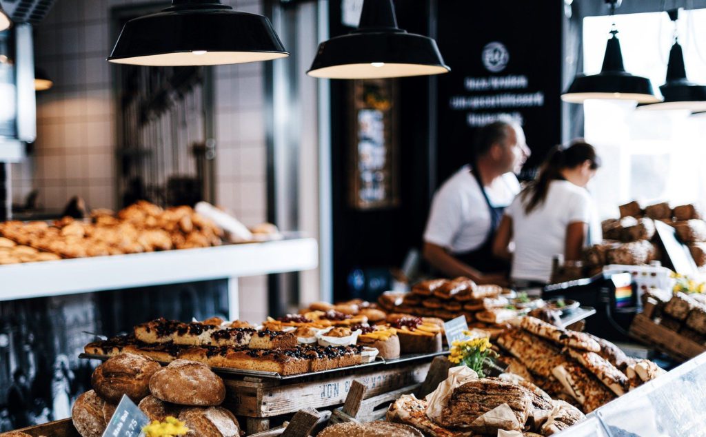 Interior of a local bakery with fresh breads, pastries, and baked goods displayed on wooden shelves with staff working behind the counter.