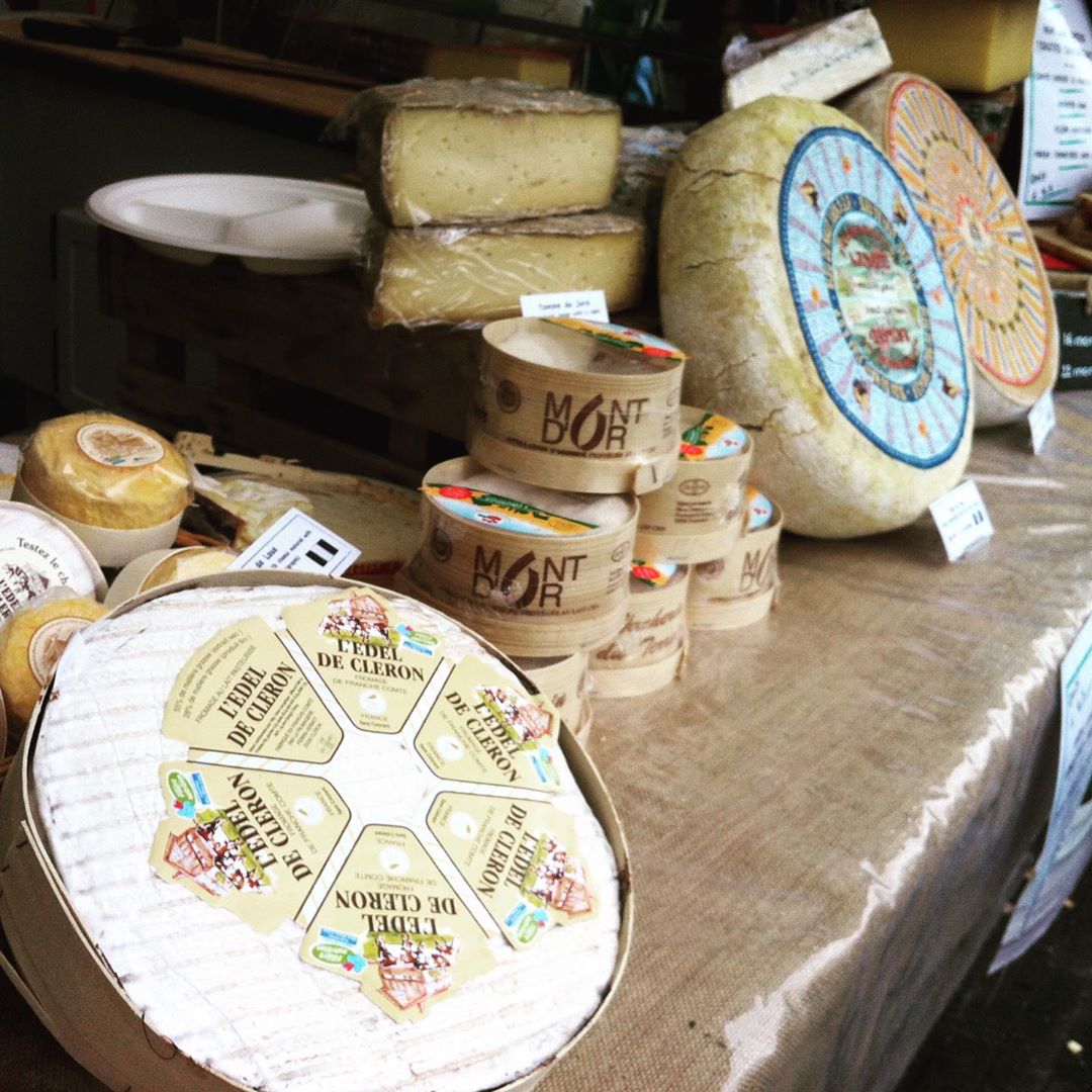 Various French cheeses displayed on a wooden surface, including wheels of Comté with traditional labels and smaller rounds of Mont d'Or cheese.